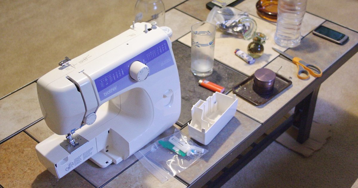 Close-up of a conventional home sewing machine, showing the needle and presser foot area with a spool of thread on top of the machine body.